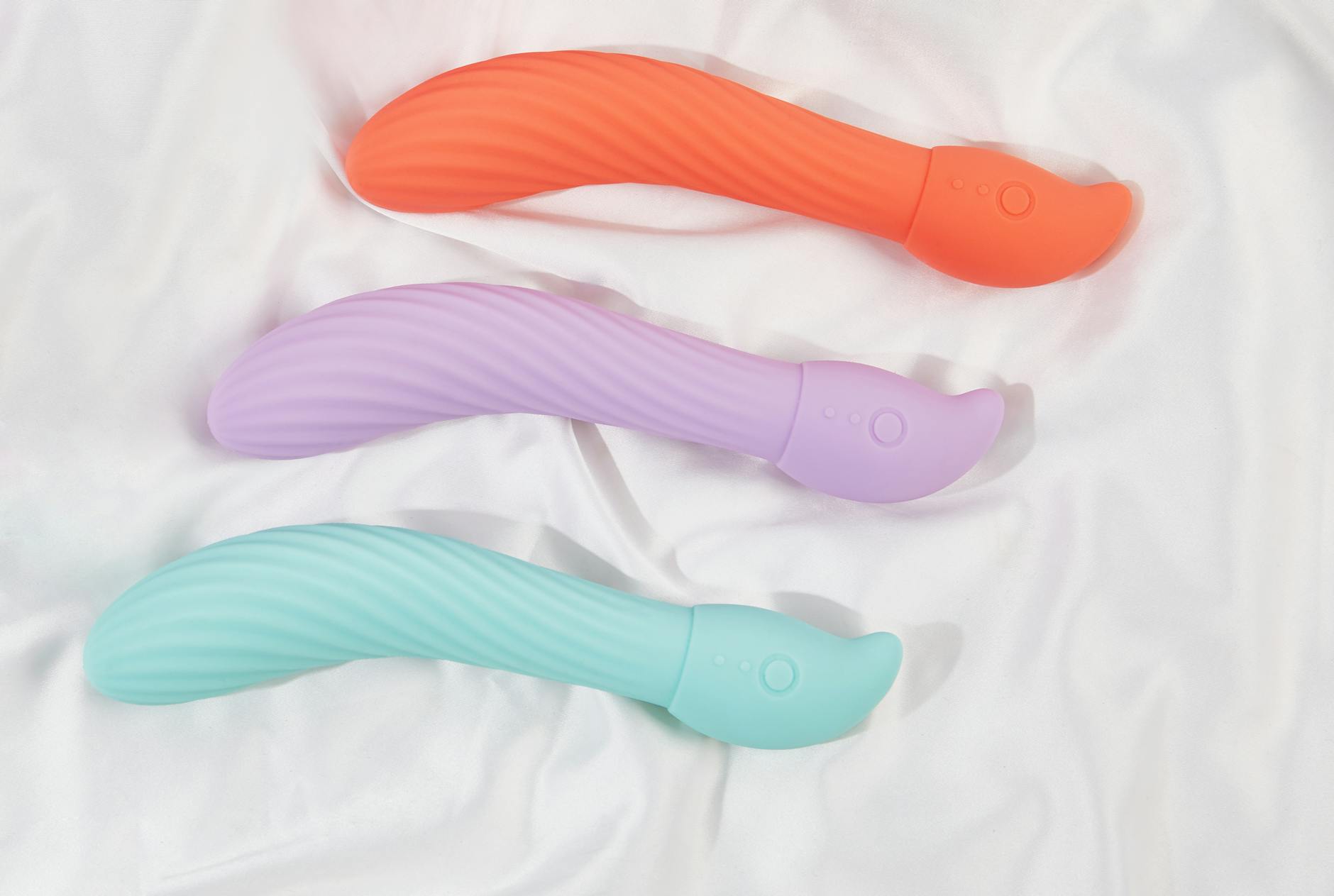 A teal silicone vibrator resting on smooth white silk, representing modern intimacy during perimenopause.