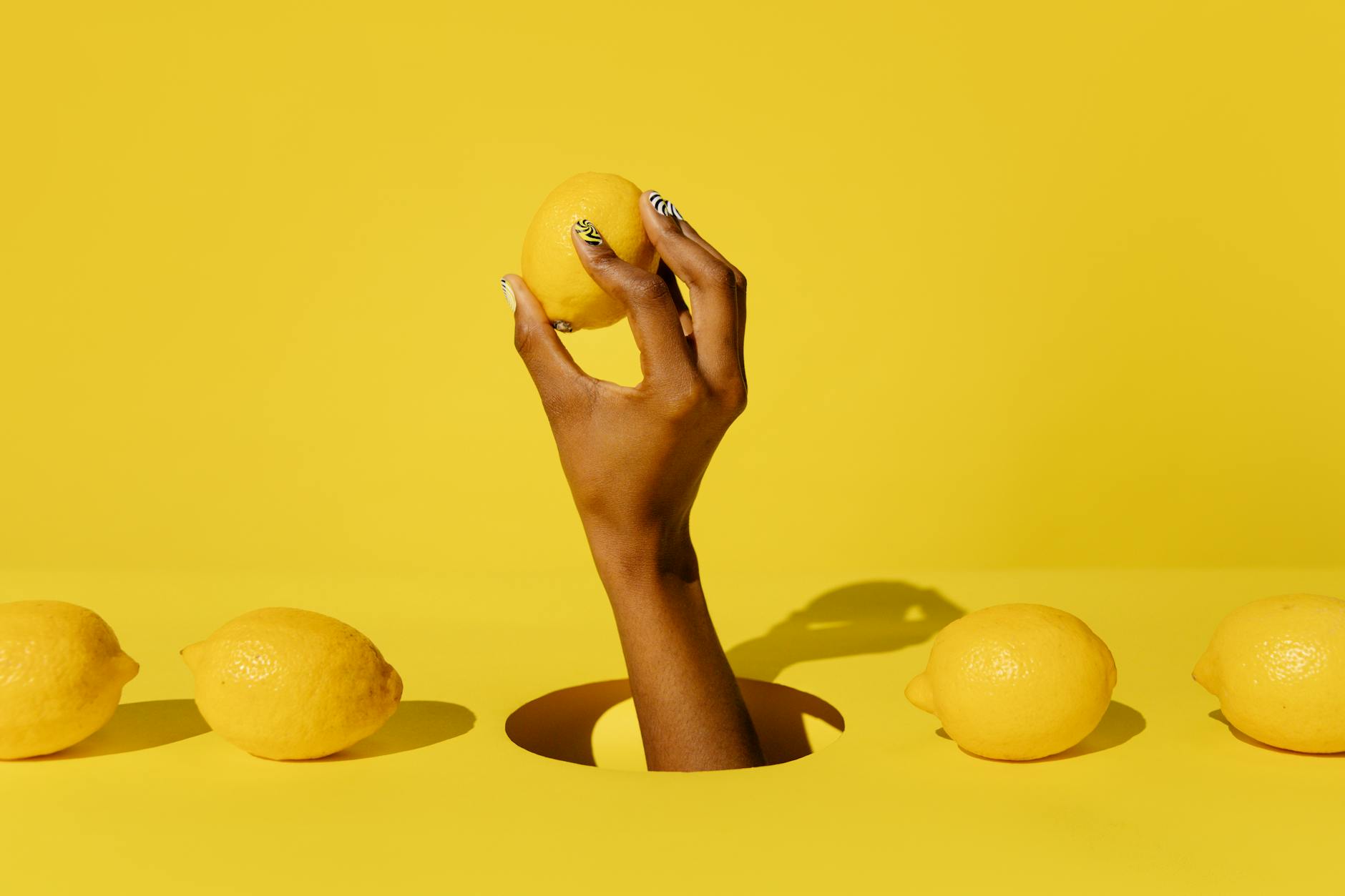 Hand holding a fresh lemon on a soft pink background with additional lemons