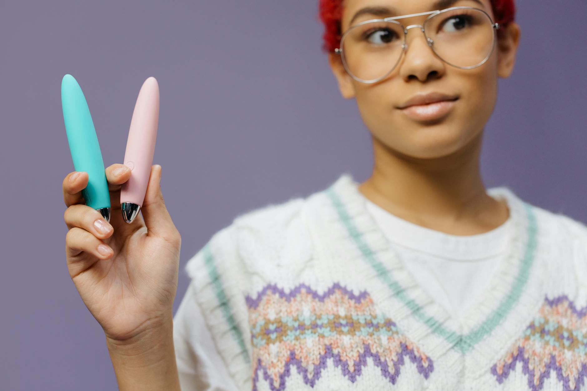 Woman holding colorful clitoral vibrators against a purple background, representing self-discovery and solo pleasure