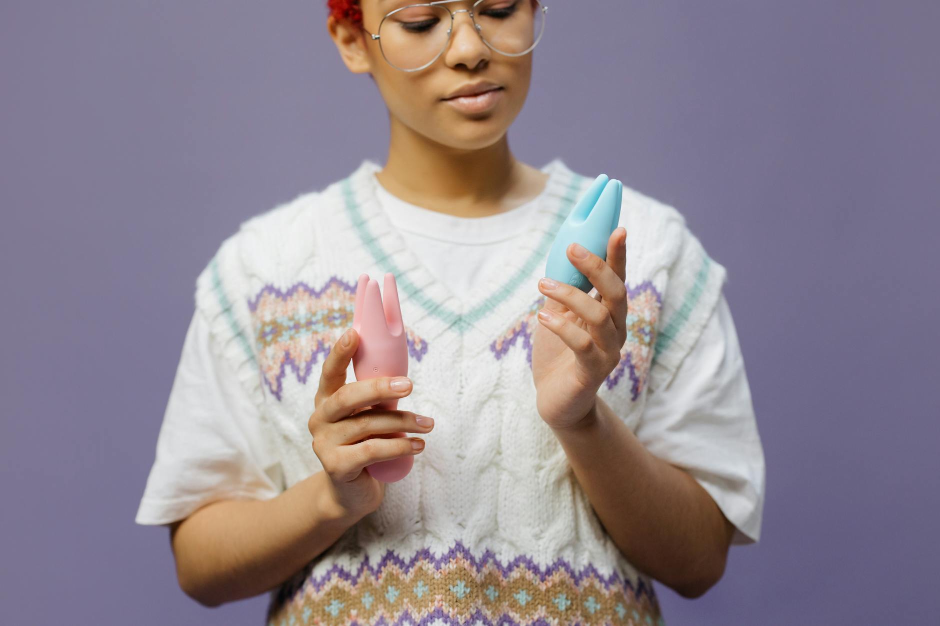 Woman holding blue and pink silicone vibrators in a contemplative moment